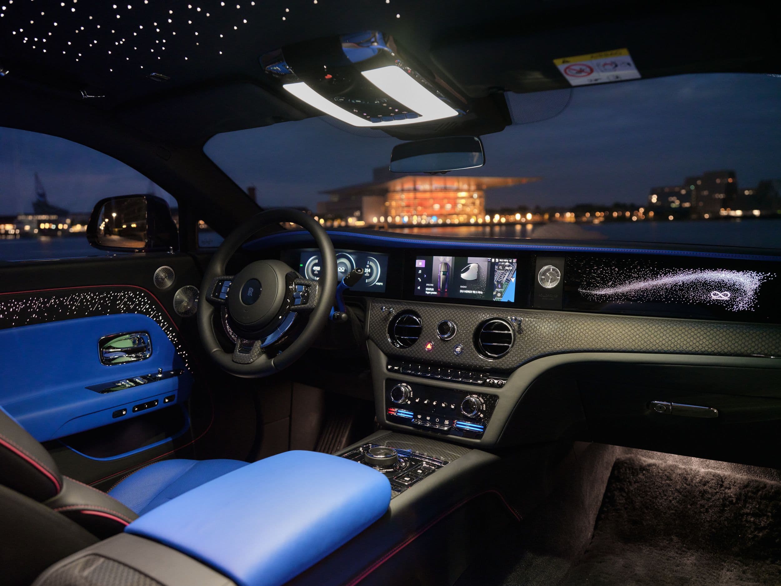 The luxurious interior of a Rolls-Royce at night, featuring blue leather seats and a starry headliner.